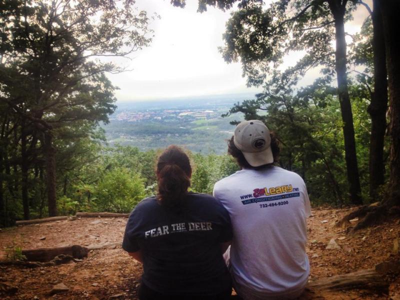 A couple sits closely together and looks down on Happy Valley from an overlook at Mt. Nittany